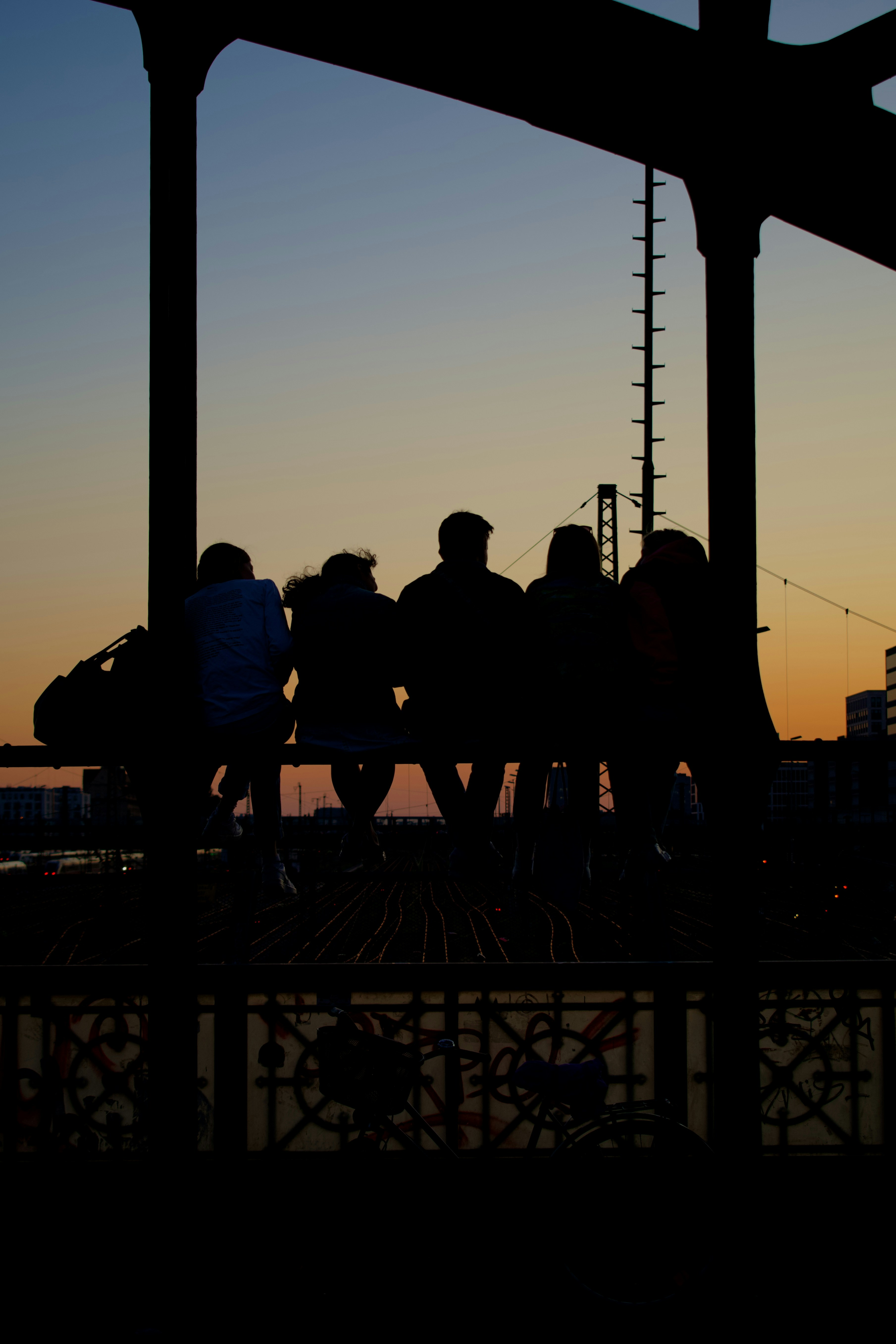 Silhouettes of a group of friends sitting on a bridge at sunset